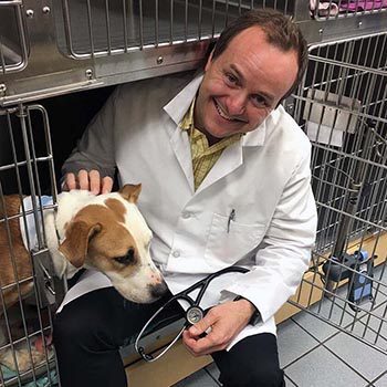 Dr. Lawrence Eden sitting with dog in kennel, smiling