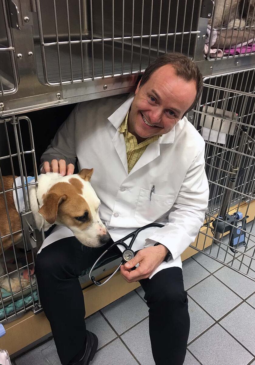 Lawrence Eden posing with dog in kennel, smiling